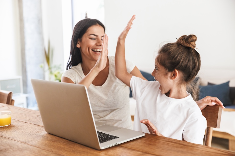 Woman high fiving child while working on laptop at home