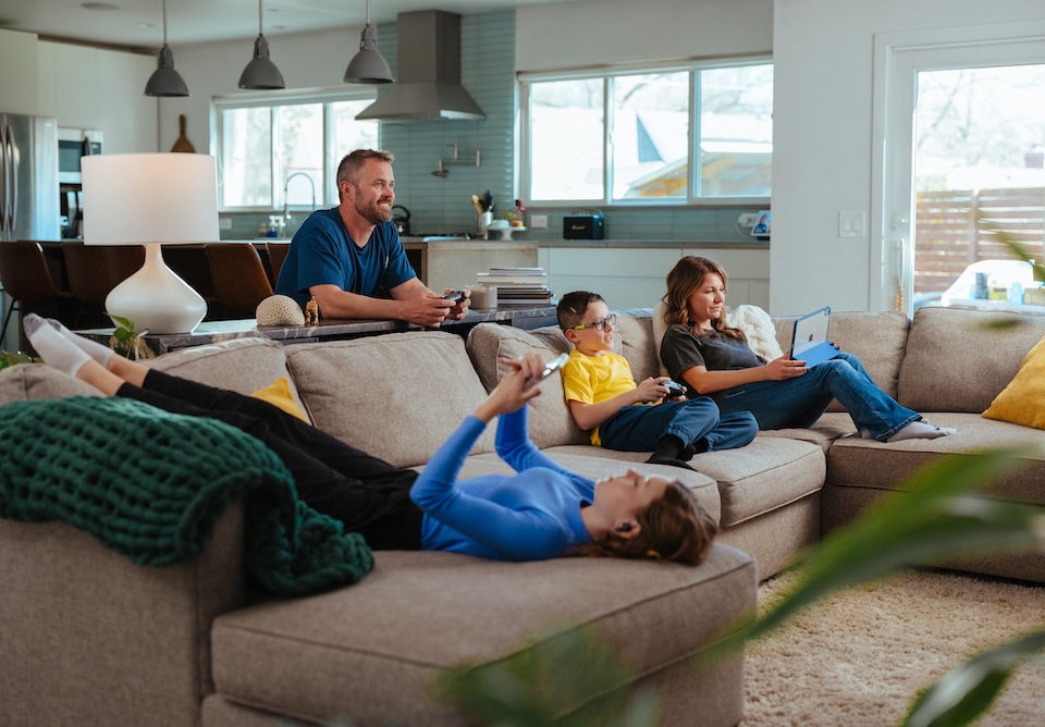 Family sitting on couch using multiple devices