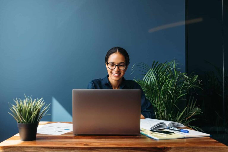 happy woman sitting at desk looking at laptop
