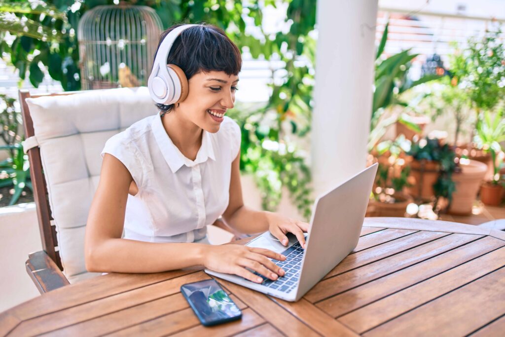 Woman on her patio outside working on her laptop with headphones on