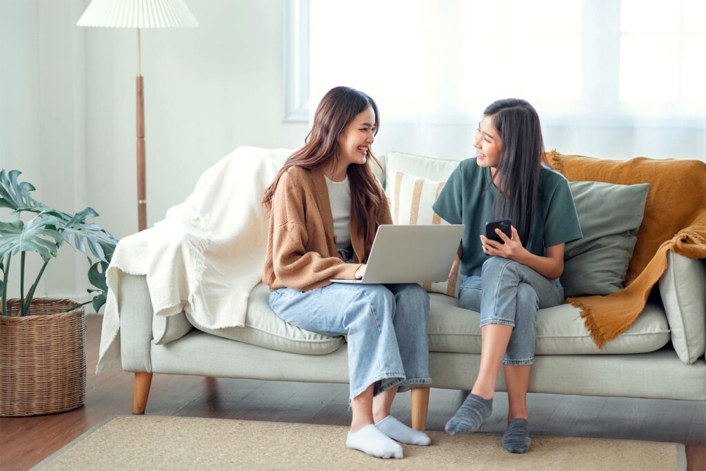 Two friends looking at a laptop and phone together