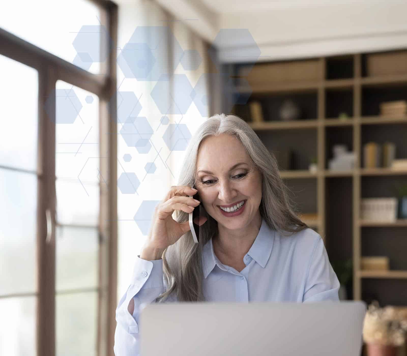 A elderly woman on a phone call while looking at her desktop computer
